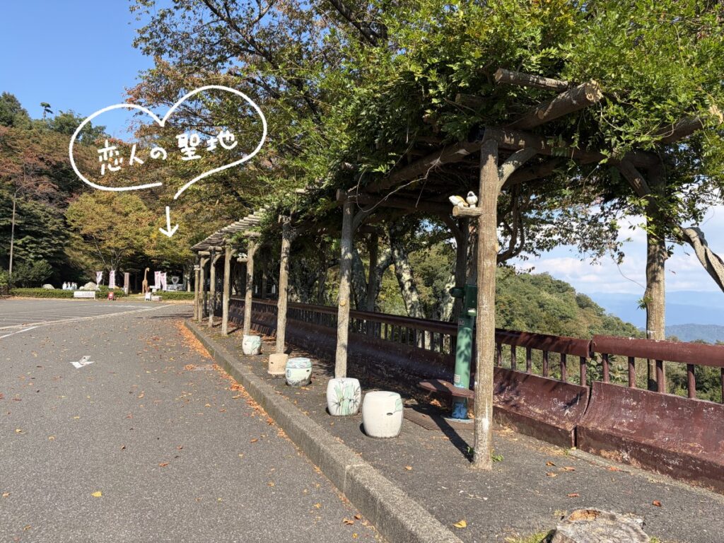 つづら尾崎展望台の藤棚と駐車場。奥の「恋人の聖地」のモニュメントを白いペンのハートと矢印で示している